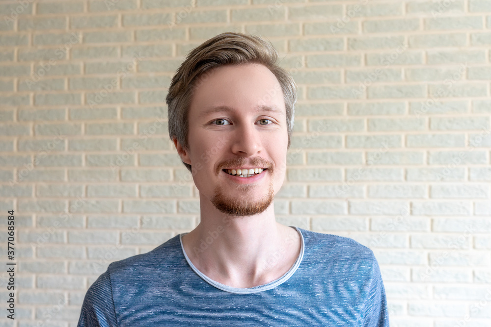 Smiling young man with red beard on brick wall background at home. Smiling young man with red beard on brick wall background at home.