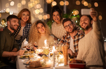 holidays, celebration and people concept - happy friends taking selfie by smartphone at home christmas dinner party