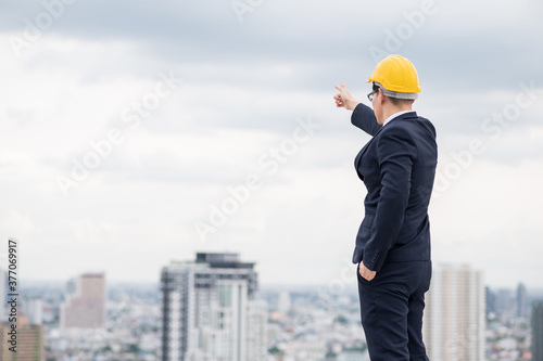 Young handsome asian civil engineer standing wearing helmet yellow hard hat in business suite on building urban cities background.