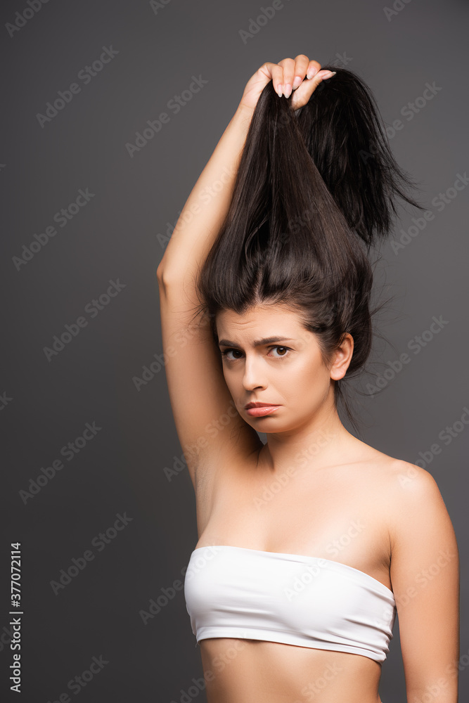 upset brunette woman holding damaged hair isolated on black upset brunette woman holding damaged hair isolated on black