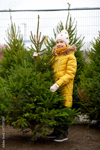 winter holidays and people concept - happy smiling little girl choosing christmas tree at street market
