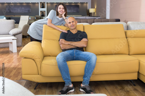 Portrait of happy couple sitting and testing new sofa in furniture store