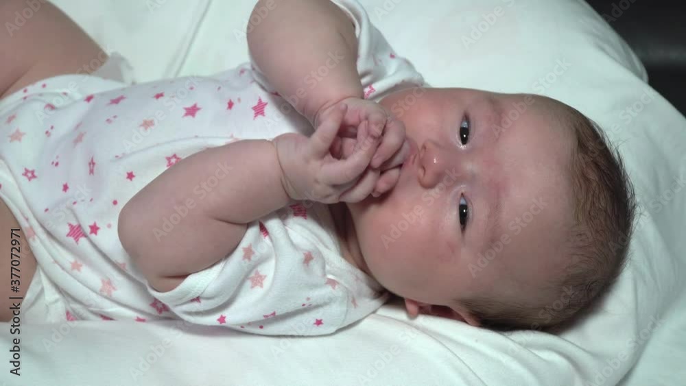 Caucasian Little cute girl lies on her back in a white bodysuit and puts her fingers in her mouth. Caucasian Little cute girl lies on her back in a white bodysuit and puts her fingers in her mouth.