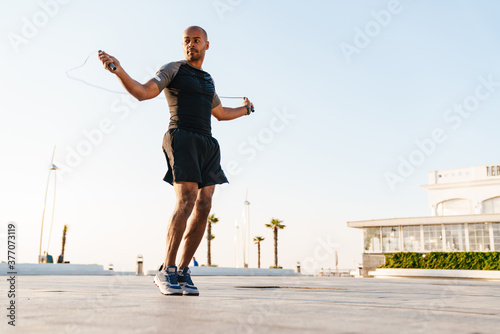 Image of athletic african american sportsman working out with jump rope