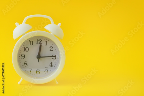 White vintage alarm clock on a bright yellow background. Clock with black arrows. Copy space, banner