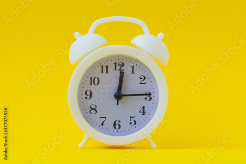 White alarm clock 12 hours 15 minutes. Bright yellow background, copy space