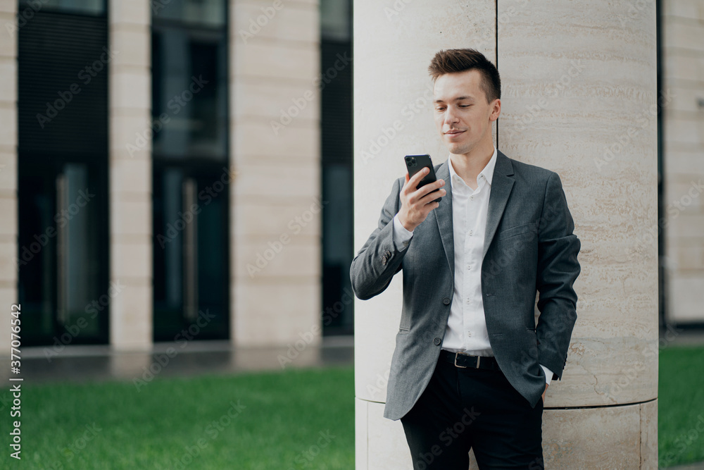 a smart strong man businessman of Caucasian appearance holds a new phone in his hands and writes a text to a friend. background business center. thinking about a good job for the future a smart strong man businessman of Caucasian appearance holds a new phone in his hands and writes a text to a friend. background business center. thinking about a good job for the future