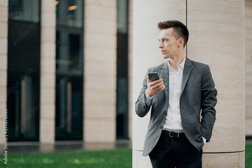 a smart man businessman of Caucasian appearance holds a new phone in his hands and writes a text to a friend. background business center. thinking about a good job for the future a smart man businessman of Caucasian appearance holds a new phone in his hands and writes a text to a friend. background business center. thinking about a good job for the future