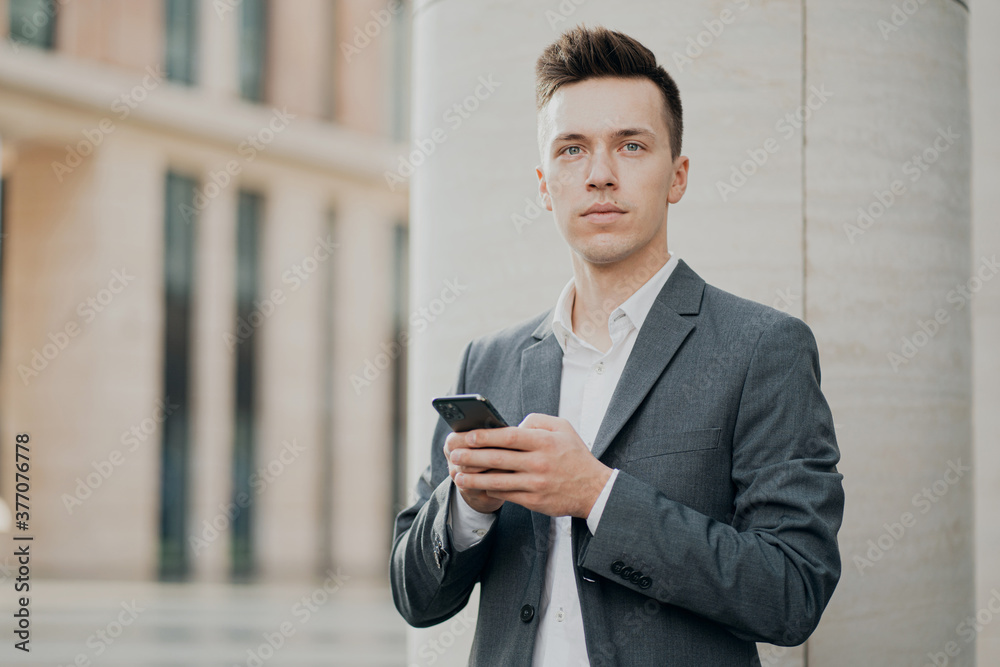 smart male student holding a new phone writes a friend a message. Grey business suit, brunette hair stylish barbershop hair salon. smart male student holding a new phone writes a friend a message. Grey business suit, brunette hair stylish barbershop hair salon.