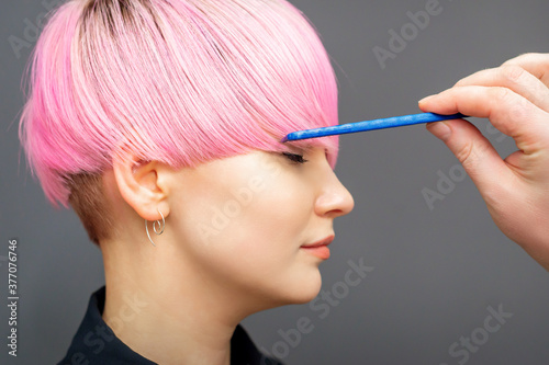 Hairdresser checking short pink hairstyle of young woman with comb on gray background