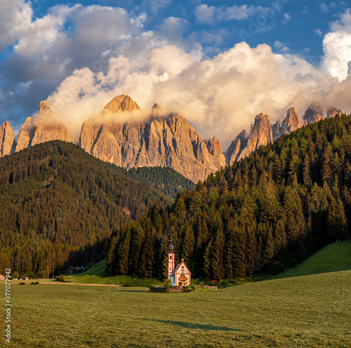 Golden hour at St. Johns church in South Tyrol, the Italian Dolomites with cloud covered Sass Rigais mountains in the background photo