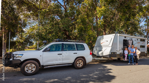 A Young Family proudly standing outside of their caravan and 4WD in front of a Park