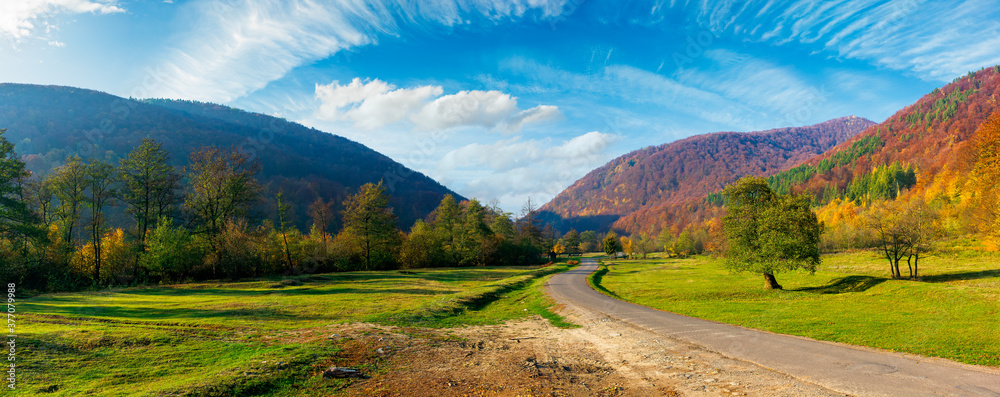 road winding through the country valley panorama. wonderful autumn landscape in mountains. forest on hills in colorful foliage. sunny weather with fluffy clouds on the sky