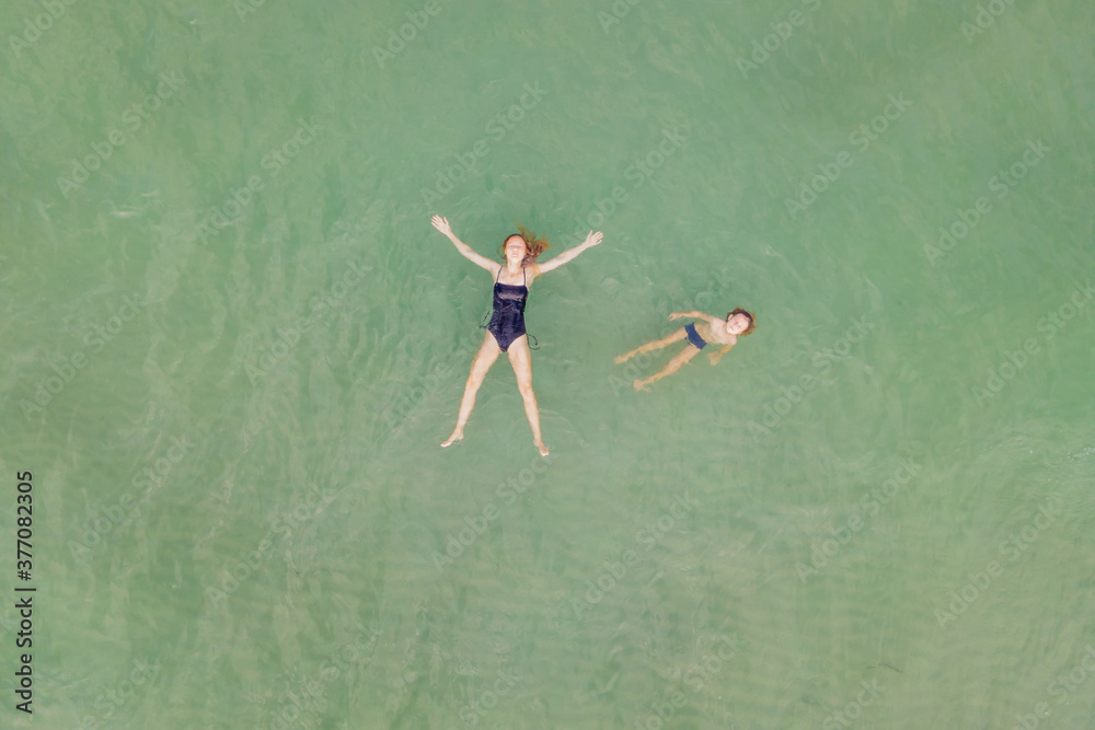 Mom and son in clear turquoise water on the beach. Drone view