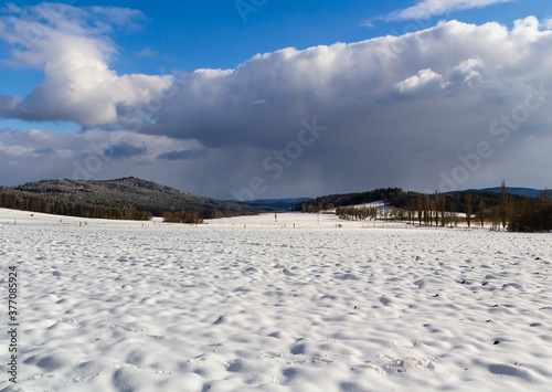 Winter czech landscape with hill, snow field and big cloud on sky
