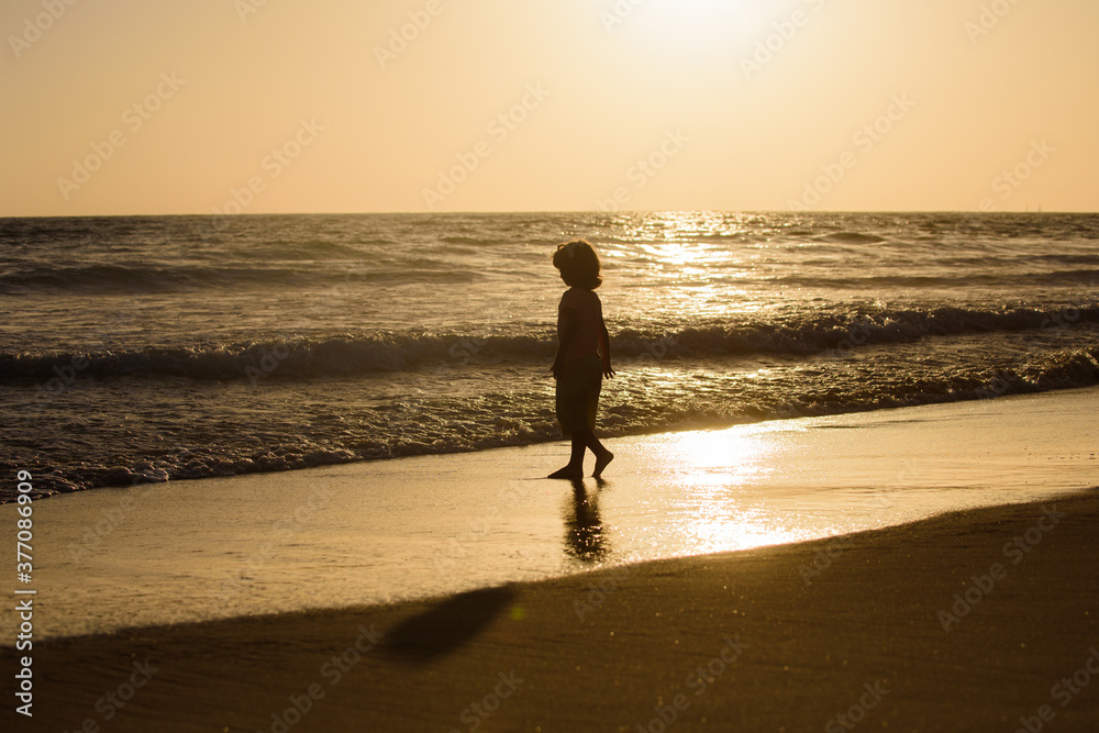 Kid running on sandy beach at sunset. Child boy having fun on the beach. Summer vacation and healthy kids lifestyle concept.