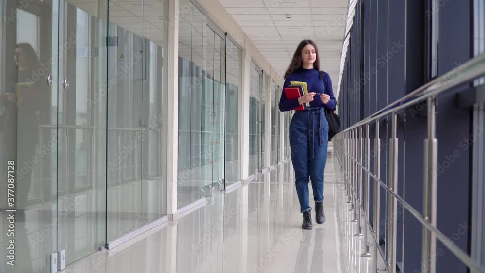Female student with a book walking in the university. Exam preparation. New modern fully functional education facility. Concept of online education Female student with a book walking in the university. Exam preparation. New modern fully functional education facility. Concept of online education