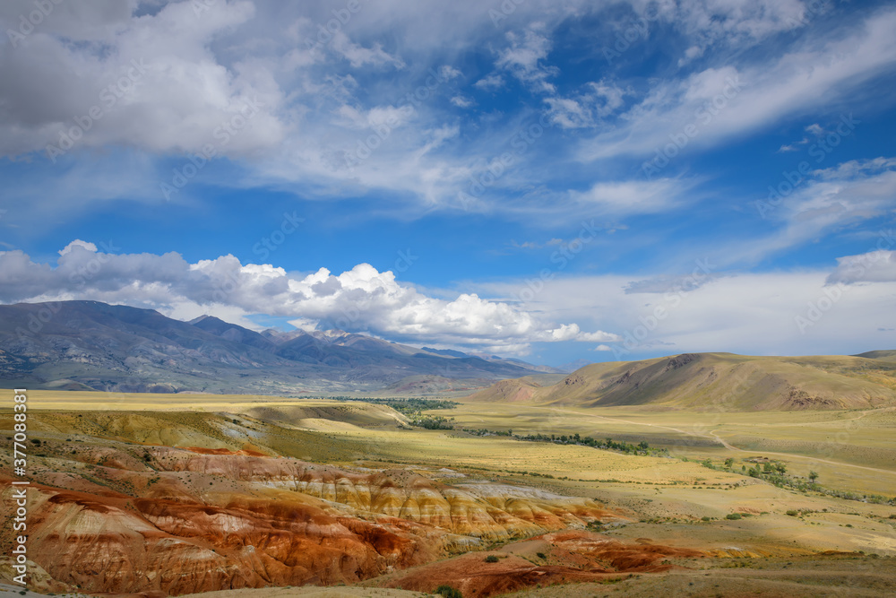 Fantastic deserted mountain landscape on sunny day. Colorful rocks under blue sky with white clouds. Wild and lost corners of the planet, Martian landscape in the Altai.