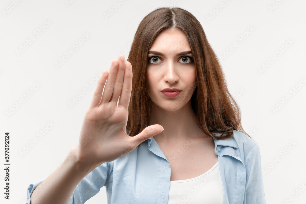 Serious girl with long chestnut hair shows a stop with her hand, not allow violence, body language Serious girl with long chestnut hair shows a stop with her hand, not allow violence, body language