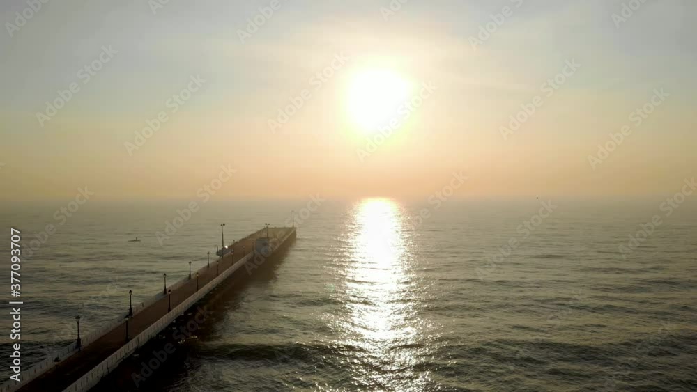 Rising aerial view of pier extending from land out over water in the vast endless ocean during golden hour. Rising aerial view of pier extending from land out over water in the vast endless ocean during golden hour.