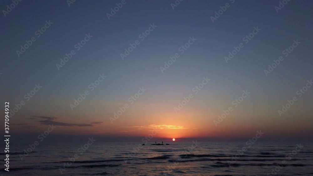 sunset on a beach. silhouette fishermen on a rock in the sea sunset on a beach. silhouette fishermen on a rock in the sea