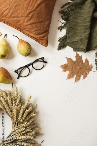 Blanket, pillow, glasses, dry autumn leaves, pears, wreath of wheat straw on white table. Fall autumn concept. Mock up, copy space, flat lay. photo