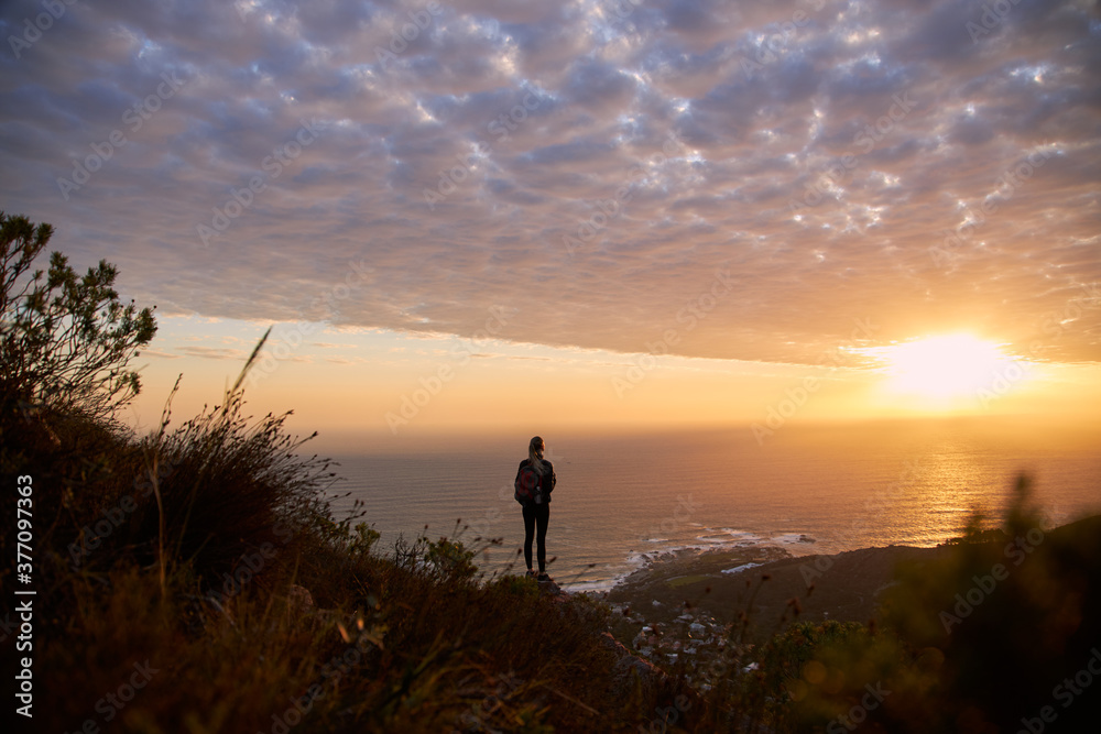 Woman watching sunset from clifftop wearing backpack