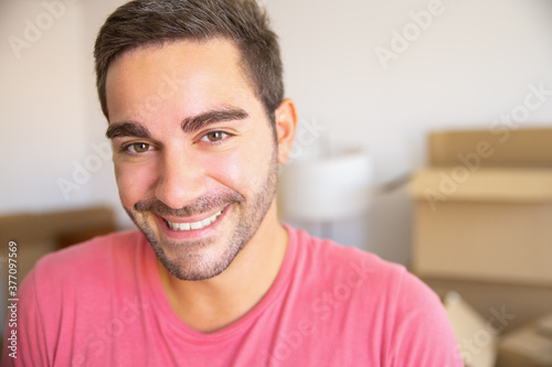 Happy young man moving in new apartment, standing in front heap of opened carton boxes, looking at camera. Closeup shot. Real estate concept