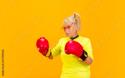 Boxing in gloves. Senior woman in ultra trendy attire isolated on bright orange background. Looks stylish and fashionable, forever young. Caucasian model in sunglasses, bright attire and sneakers © master1305