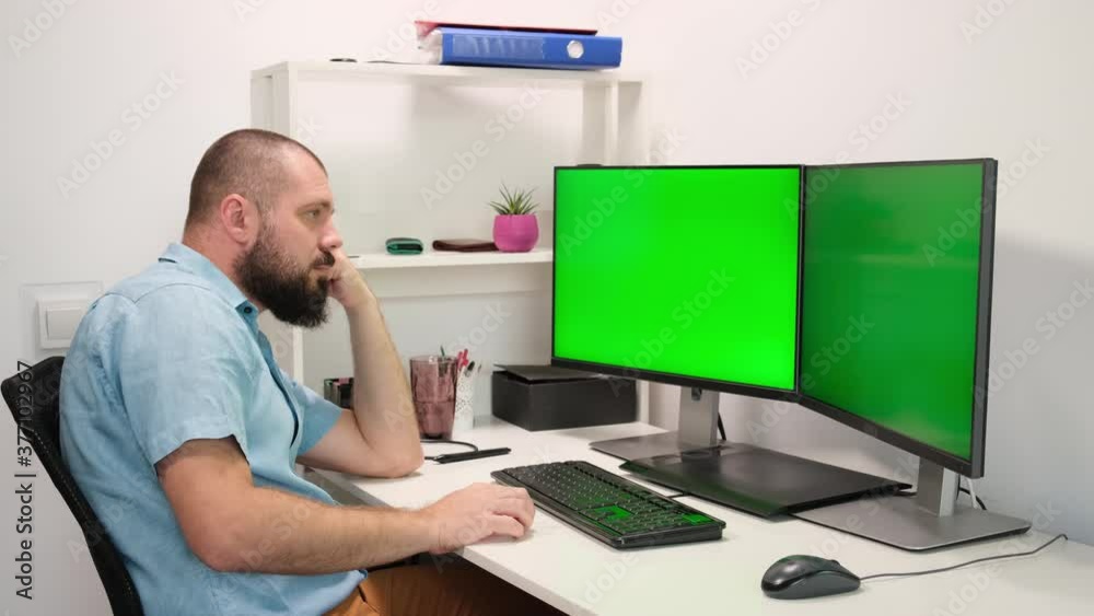 a man working at home in front of two green monitors. a man thinks and he has an idea. a man working at home in front of two green monitors. a man thinks and he has an idea.