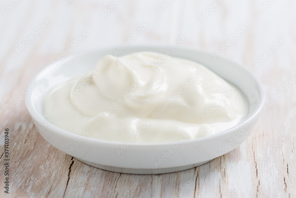 Organic white yogurt or sour cream in bowl on white wooden background Organic white yogurt or sour cream in bowl on white wooden background