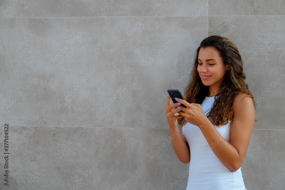 Fototapeta premium Young beautiful woman of Arabic ethnicity wearing tight white dress standing near the grunged concrete textured wall. Close up, copy space, background.