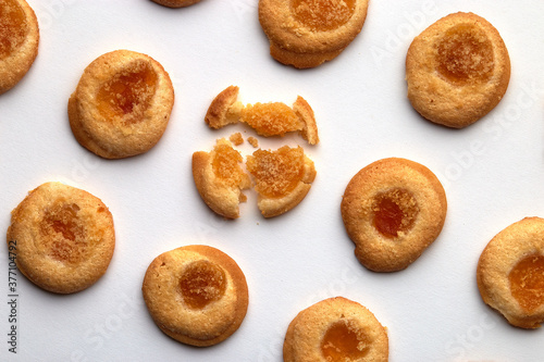 Nine handmade cookies with apricot jam arranged in even rows from an angle. One in the center is broken. on white background