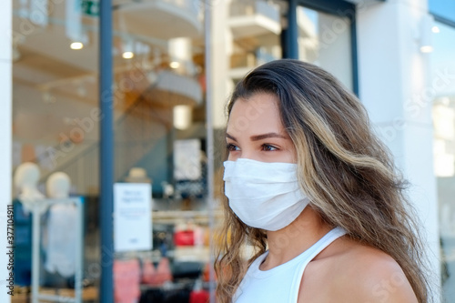 Portrait of young beautiful woman of Arabic ethnicity wearing disposable face mask as barrier to protect against contact with infectious materials at the streets. Close up, copy space, background.