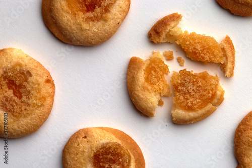 Four handmade cookies with apricot jam arranged in even rows from an angle. One in the center is broken. on white background