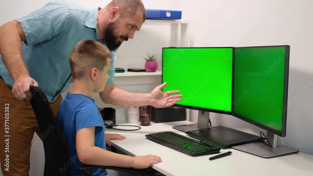 father and son do homework remotely in front of two green monitors. the man explains the new material to the child. father and son do homework remotely in front of two green monitors. the man explains the new material to the child.