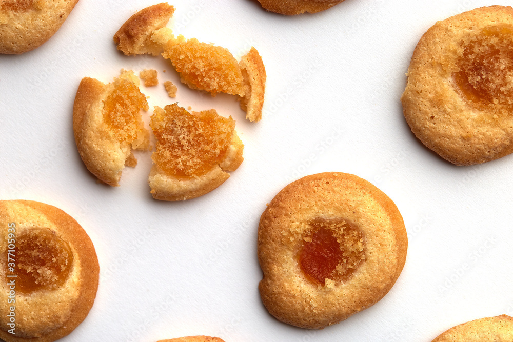 Four handmade cookies with apricot jam arranged in even rows from an angle. One in the left corner is broken. on white background