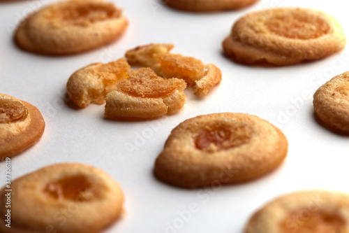 Five handmade cookies with apricot jam arranged in even rows from an angle. One in the center is broken. on white background