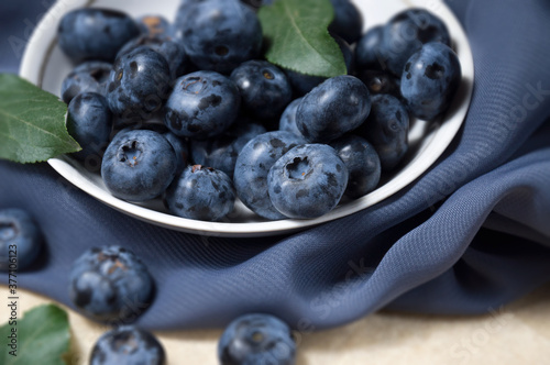 Freshly picked ripe blueberries in a white plate on a gray cloth. Selective focus. Harvest berries. Healthy eating.