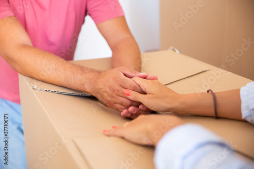 Man and woman supporting each other and holding hands over cardboard pack, while moving into new apartment. Closeup of female and male arms on carton box. Cropped shot. Relocation or new home concept © Mangostar