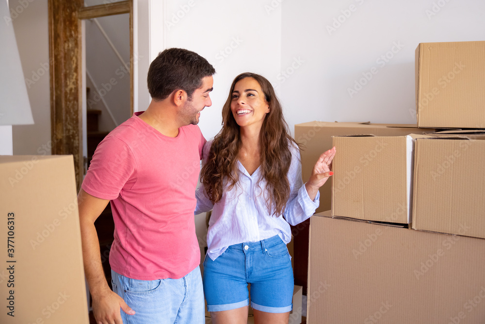 Cheerful family couple standing among carton boxes, hugging and discussing their new apartment. Medium shot. New home concept Cheerful family couple standing among carton boxes, hugging and discussing their new apartment. Medium shot. New home concept