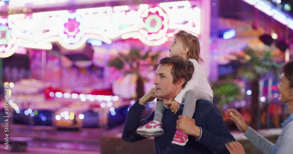 Authentic shot of a happy smiling family is having fun together in amusement park with luna park lights at night.
