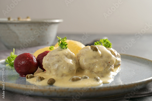 Boiled meatballs in white sauce with capers, in Germany called Koenigsberger Klopse, with beetroot, potatoes and parsley garnish on a gray plate, copy space, close-up with selected focus photo