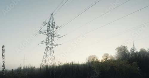 High voltage lines and power pylons in a flat and green agricultural landscape, green floral background with morning sky