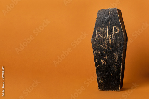 Toy homemade wooden black coffin on an orange background. Festive halloween composition with copy space.