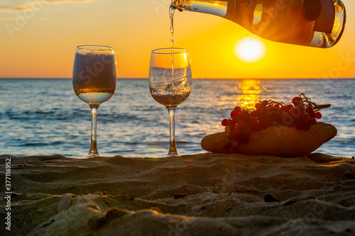 Fototapeta Naklejka Na Ścianę i Meble -  Two glasses of champagne and grapes on sandy beach at sunset, Sicily island, Italy