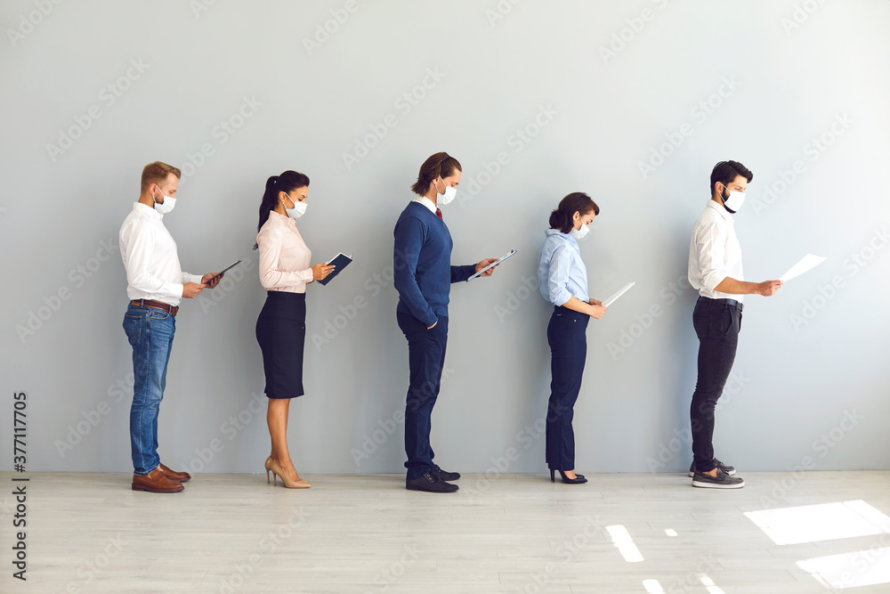 Obraz premium Group of business people in masks standing with documents in line and keeping distance in office