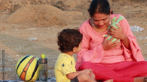 Indian mom making her baby child playing with blue teddy near sea shore in india