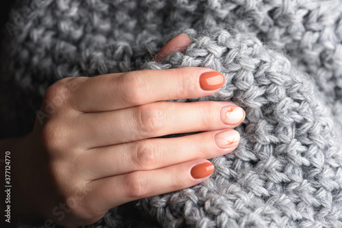 Female hands with trendy autumn marble manicure in orange color. Grey knitted wool sweater or plaid