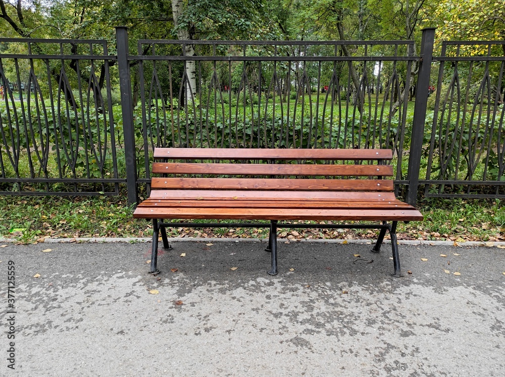 Public wooden brown bench in the city park. Damp bench surface from the rain. A Quiet Bench at the green square. Public wooden brown bench in the city park. Damp bench surface from the rain. A Quiet Bench at the green square.